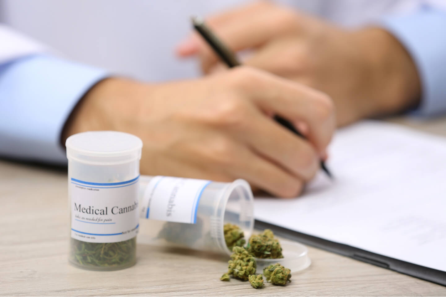 Cannabis Patient werden Medical Cannabis Rezept mit Cannabis-Blüten in Apotheken-Dosen, Hand mit Stift im Hintergrund
